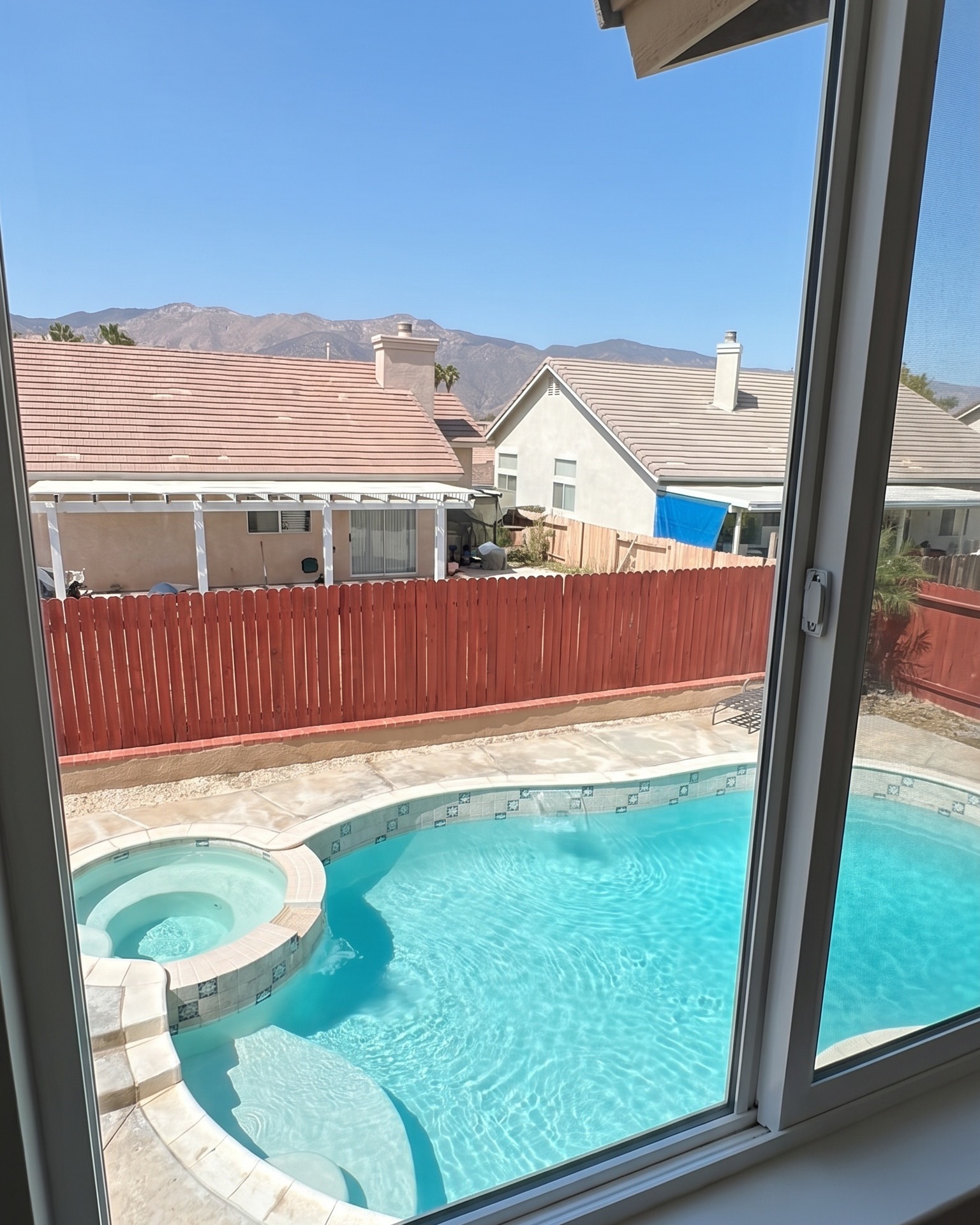Open sliding window looking down over a backyard pool and the mountains